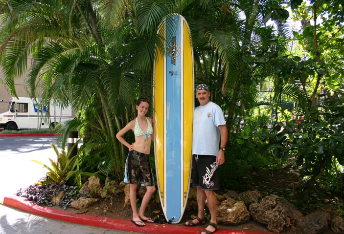 A man and woman standing next to a surfboard.