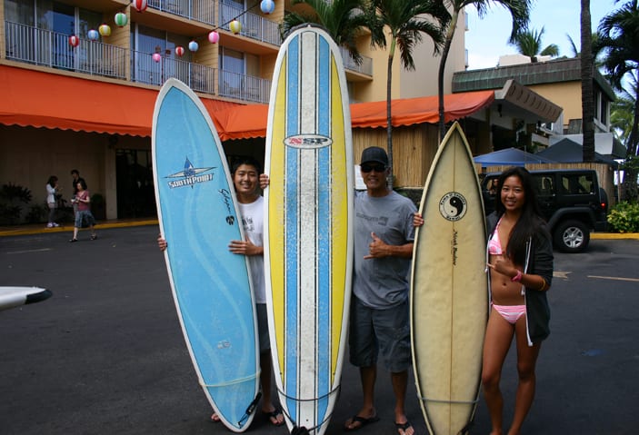 Three people standing next to surfboards in front of a hotel.