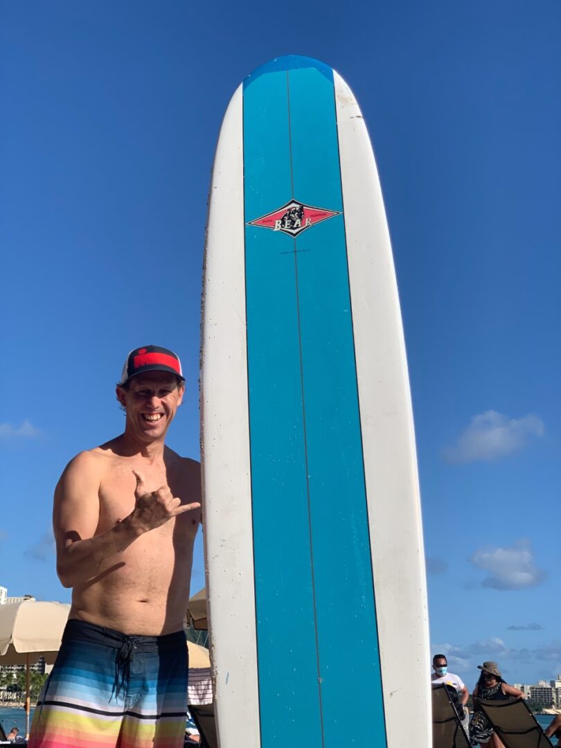 A man standing next to a surfboard in the sun.