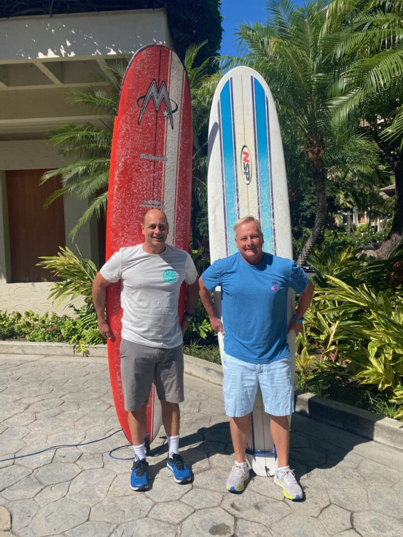 Two men standing next to each other holding surfboards.